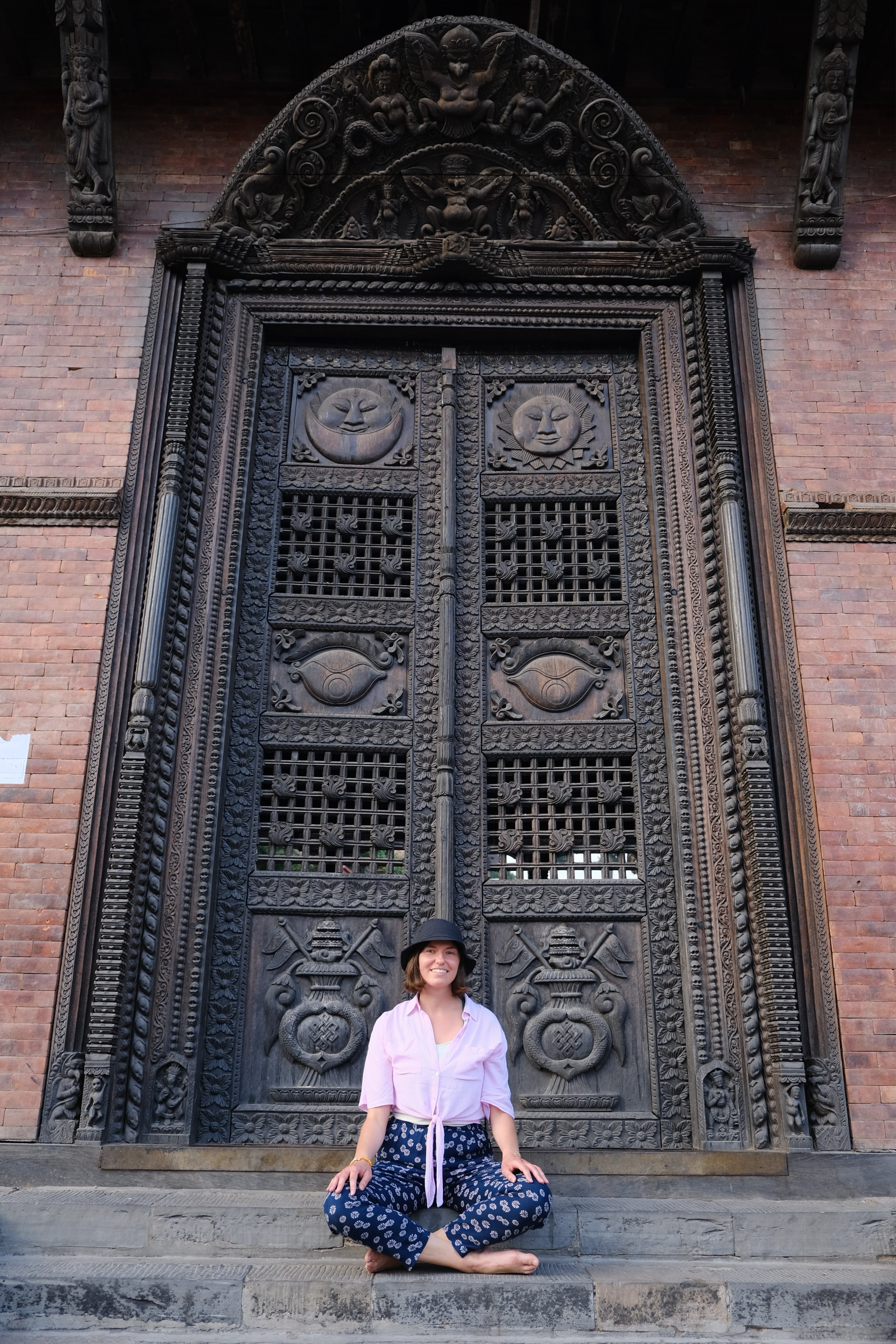 Maggie sitting cross-legged in front of an ornately carved Nepalese temple door